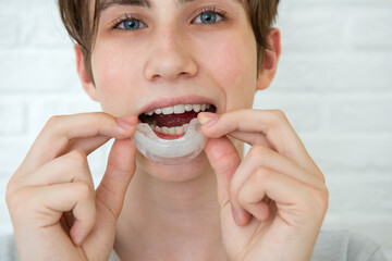 Positive teen boy holds mouth guards for her teeth. Orthodontic silicone transparent teeth aligner in hands. Dental care