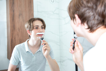 Teenage boy using a bathroom mirror to shave in the morning