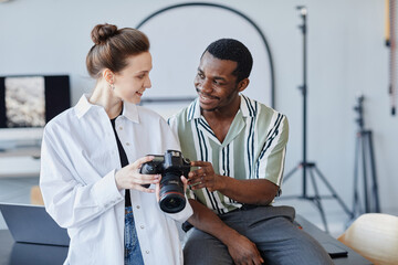 Minimal waist up portrait of two young photographers looking at images in camera and smiling