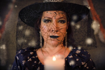 Woman costumed as a witch holding lighted candle.