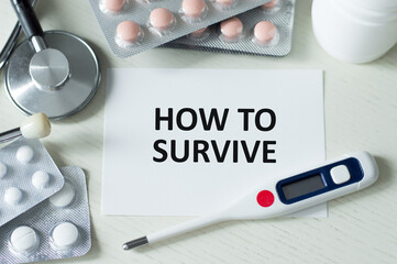 HOW TO SURVIVE text on a card on a table next to a stethoscope and thermometer, tablets