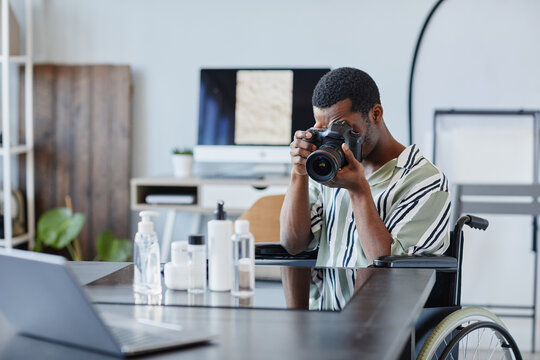 Portrait of young black man as photographer with disability taking product pictures in photo studio