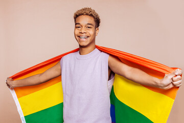 Portrait of cheerful afro latin american young man with a gay rainbow pride flag at studio over...