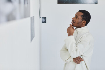Fototapeta premium Side view portrait of handsome black man looking at images in photo gallery and enjoying art, copy space