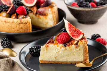 A piece of homemade baked cheesecake with fruits and berries: figs, strawberries and blackberries,  on a black plate.
