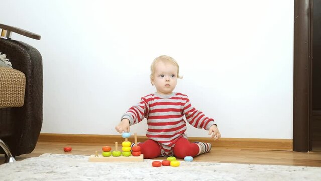 Funny caucasian blonde baby girl playing with wooden educational toys at home on the floor