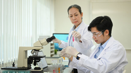 Fototapeta premium Middle age female scientist and laboratory assistant conducting experiment with test tubes and microscope slides in laboratory