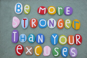 Be stronger than your excuses, creative slogan composed with multi colored stone letters over green sand