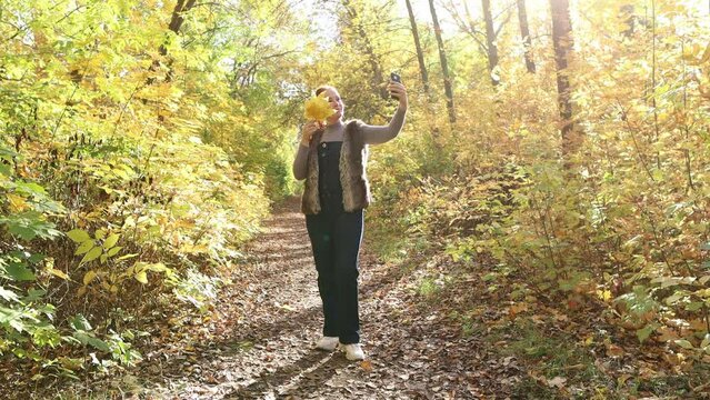 a red-haired woman with yellow leaves in her hands in an autumn park takes a selfie.