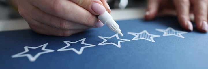 Female hand crossing out service quality rating stars with white marker closeup