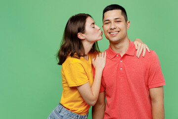 Fototapeta premium Young fun smiling happy couple two friends family man woman wear basic t-shirts together girlfriend kiss cheek face hug boyfriend isolated on pastel plain light green color background studio portrait.