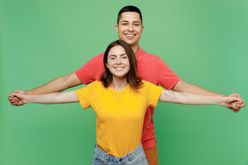 Young couple two friends family man woman wear basic t-shirts together boyfriend stand behid girlfriend hold outstretched hands lik fly isolated on pastel plain light green color background studio.