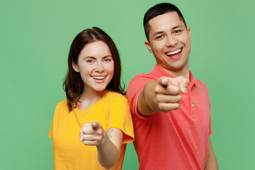 Young fun confident leader couple two friends family man woman wear basic t-shirts together point index finger camera on you motivating encourage isolated on pastel plain light green color background.