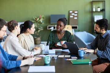 Confident African American businesswoman with palette explaining her opinion to colleagues while looking at one of them at meeting