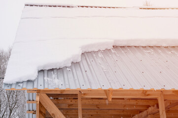 snow sliding down from roof. building construction house with metal roof covered fresh icy frozen snow and snowflakes on frosty winter day in village suburb. snowy winter season. cold weather. flare