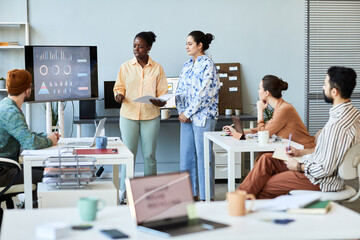 Young confident teacher or coach standing in front of audience at seminar and explaining main...