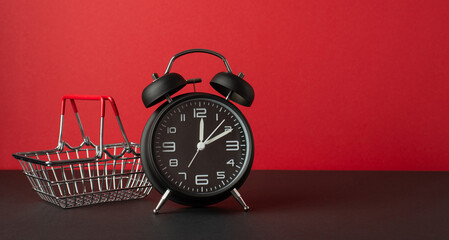 Black friday concept. Photo of black alarm clock and shopping cart on black table red wall...