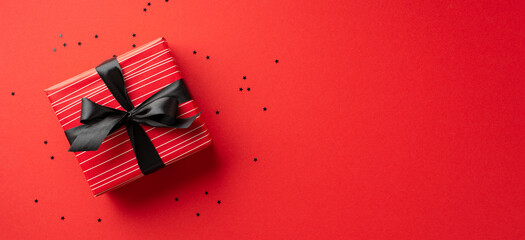 Fototapeta na wymiar Black friday sales concept. Top view photo of big red giftbox with black ribbon bow and confetti on isolated red background with copyspace