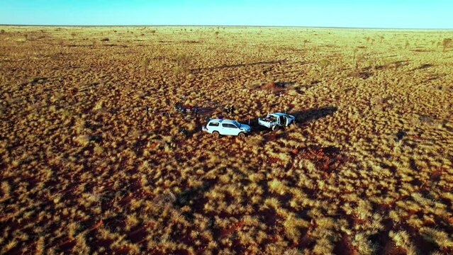 Circling aerial footage of cars and people packing up their swags in the Tanami Desert