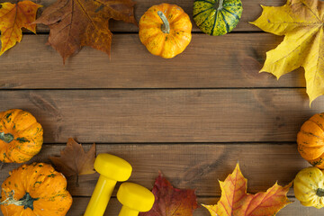 Two yellow dumbbells, small autumn pumpkins on fall leaves. Healthy fitness lifestyle composition...