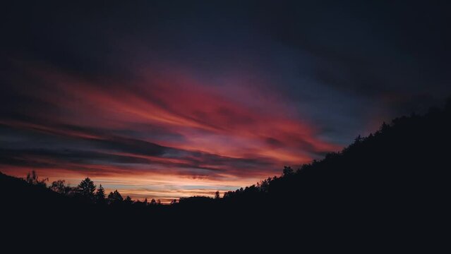 Camera rises high above the black forest and reveals a beautiful red sky after sunset. Drone, revealing shot. Copy space