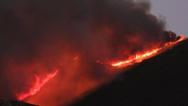 Large and uncontrollable fire in forest on silhouetted mountain
