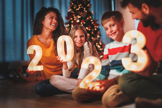 Parents and children holding illuminative numbers 2023 while celebrating New Year