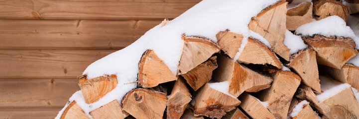 textured firewood background chopped wood for kindling and heating. woodpile stacked firewood birch tree covered fresh icy frozen snow and snowflakes. cold weather and snowy winter time season. banner