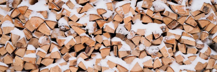 Keuken spatwand met foto getextureerde brandhout achtergrond gehakt hout voor aanmaakhout en verwarming. houtstapel gestapeld brandhout berk bedekt verse ijzige bevroren sneeuw en sneeuwvlokken. koud weer en besneeuwde wintertijd. banier © Ksenia