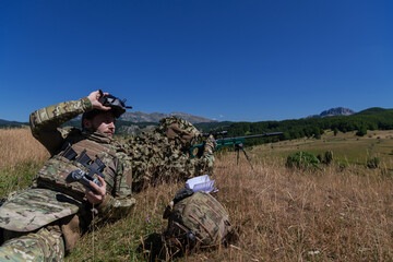 Sniper soldier assisted by an assistant to observe the area to be targeted with modern warfare tactical virtual reality goggles aerial drone military technology.