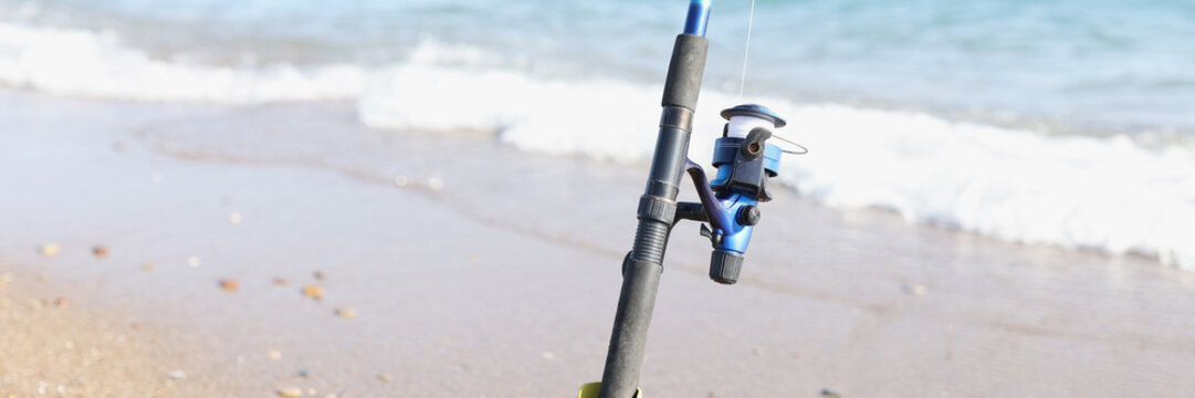 The fishing rod stands on the sand on the seashore, blurry
