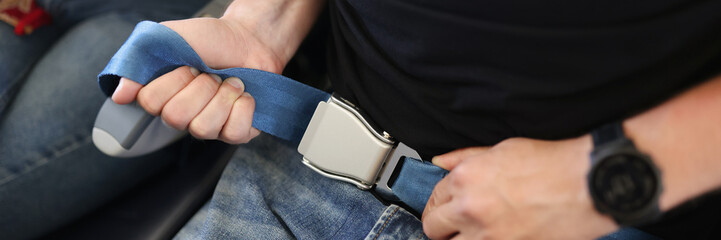 A man in jeans fastens a seat belt in an airplane