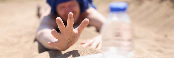 A thirsty man lies on the sand reaching for a bottle of water - obrazy, fototapety, plakaty