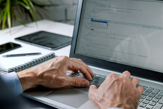 programmer writing code on laptop computer in office. website programming, software development. coder working