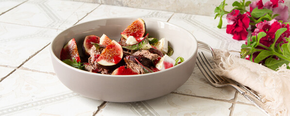 bowl of salad with duck breast and figs with raspberry sauce on the table