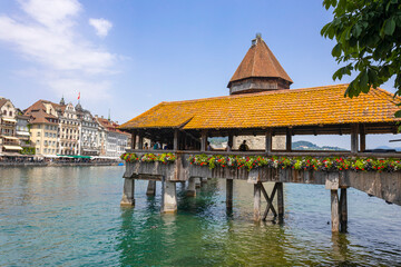 Obraz premium LUCERNE, SWITZERLAND, JUNE 21, 2022 - View of the wodden covered Kapellbrucke Bridge on the Reuss river and buildings in city center of Lucerne, Switzerland
