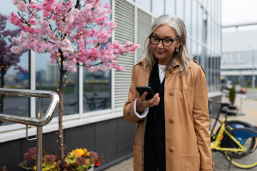 stylish elderly woman with a mobile phone in her hands in the city