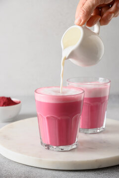 Pouring frothed milk in to beetroot latte in glass on gray background. Trendy healthy vegan drink. Vertical format.