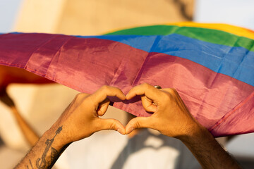 Hands making heart sign in front of rainbow flag..