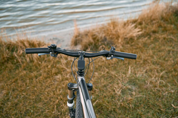 Naklejka na ściany i meble Summer evening on the lake. Close-up of a bicycle handlebar in front of a river background. Countryside adventures at the sunset.