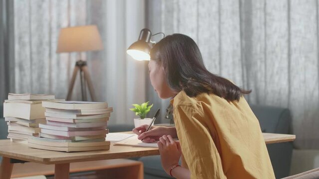 Side View Of Young Asian Female Writing On The Book While Studying At Home
