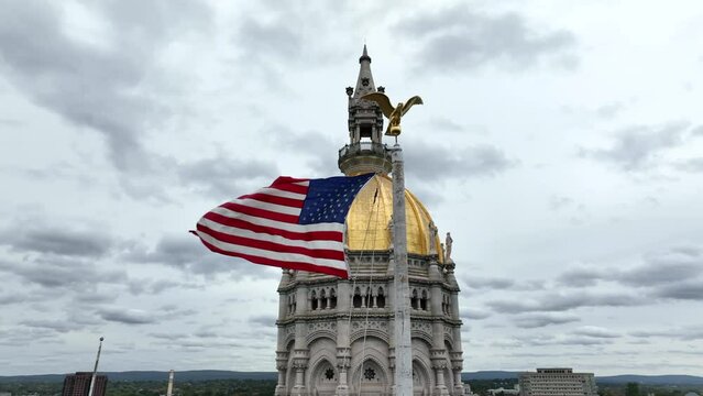 American flag waves by Hartford Connecticut state capitol dome. Aerial in Bushnell Park.