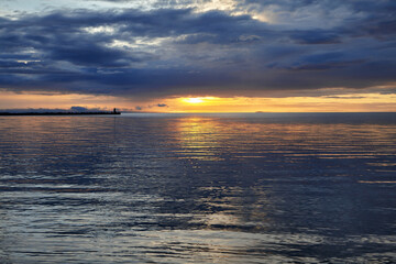 Dramatic sunset with thunderclouds before the storm. Sea pier with a lighthouse against the backdrop of the setting sun