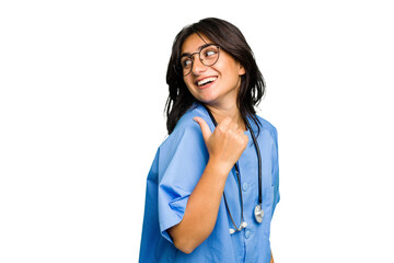 Young nurse Indian woman isolated points with thumb finger away, laughing and carefree.