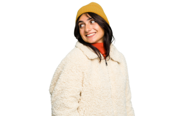 Young Indian woman wearing winter jacket and a wool cap isolated looks aside smiling, cheerful and pleasant.