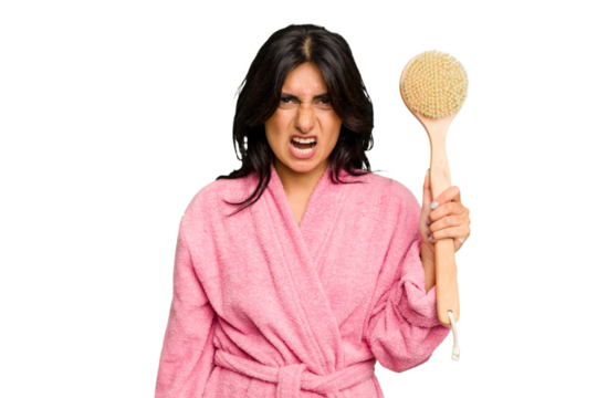 Young Indian woman in a bathrobe holding a back scratcher isolated screaming very angry and aggressive.