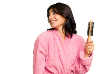 Young Indian woman in a bathrobe holding an hairbrush isolated looks aside smiling, cheerful and pleasant.