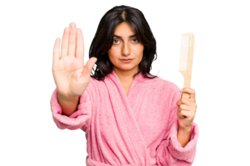 Young woman in a bathrobe holding an hair comb isolated standing with outstretched hand showing stop sign, preventing you.