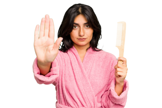 Young woman in a bathrobe holding an hair comb isolated standing with outstretched hand showing stop sign, preventing you.