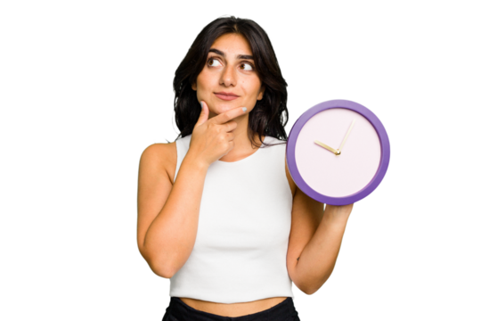 Young Indian woman holding a clock isolated looking sideways with doubtful and skeptical expression.